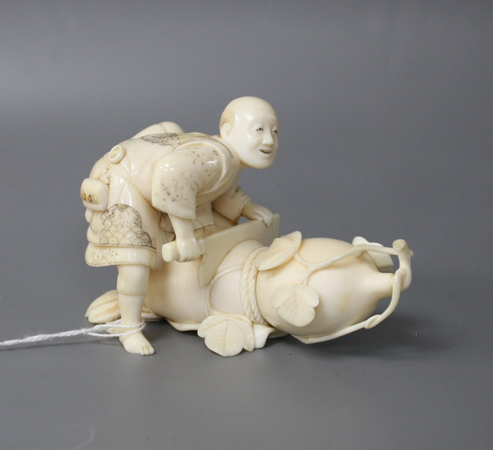 A Japanese Meiji period ivory okimono carved with a man carving a giant gourd, signed, length 10cm, height 7cm
